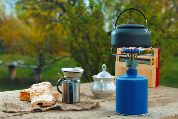 Snack outdoor in summer evening. Camping kettle, cups and biscuit on rustic table.