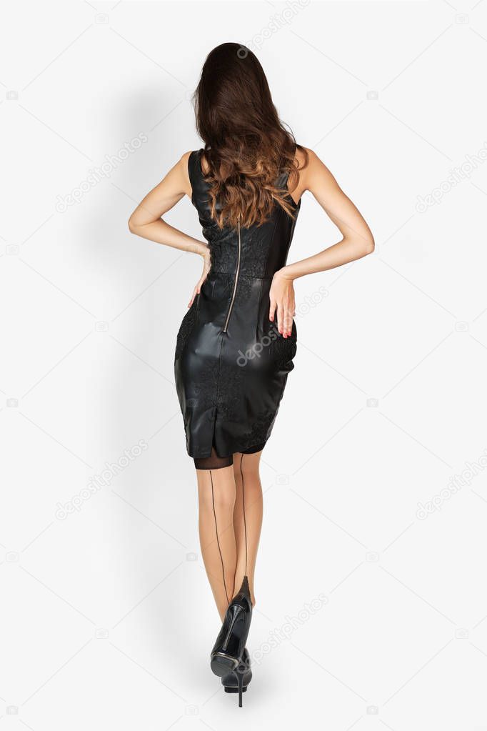 Back view of slender lady with long hair in eco leather dress raising one leg