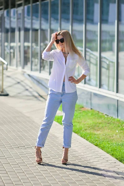 Street style fashion - lady in white shirt and boyfriend jeans walking along business centre — Stock Photo, Image