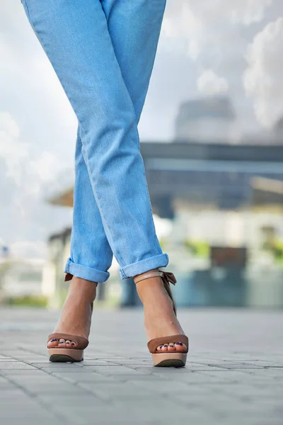 Crossed female legs in blue jeans and suede shoes on pavement