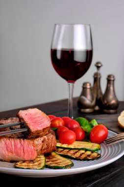 Izgara sığır biftek ve kabak taze domates kiraz ve fesleğen ve kırmızı şarap bir bardak ile servis
