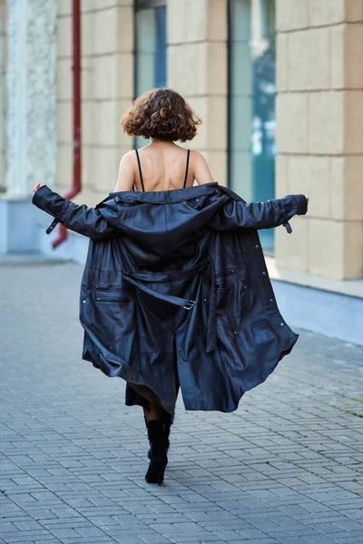 Back view of a lady walking down the street and taking off leather coat — Stock Photo, Image