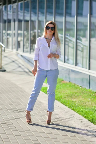 Мода уличного стиля - дама в белой рубашке и джинсах бойфренда, гуляющая по бизнес-центру — стоковое фото