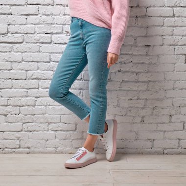 Turkuaz kot pantolon, pembe kazak ve beyaz tuğla duvara yaslanmış spor ayakkabı kadın bacaklar
