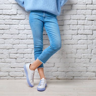 Mavi kot pantolon, kazak ve beyaz tuğla duvara yaslanmış spor ayakkabı kadın bacaklar