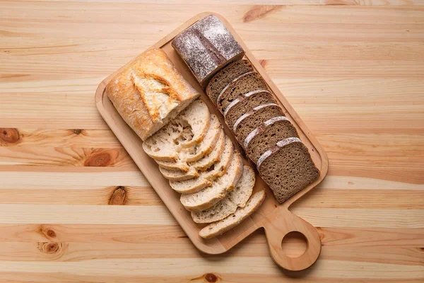 Bovenaanzicht van wit en bruin brood op houten snijplank — Stockfoto