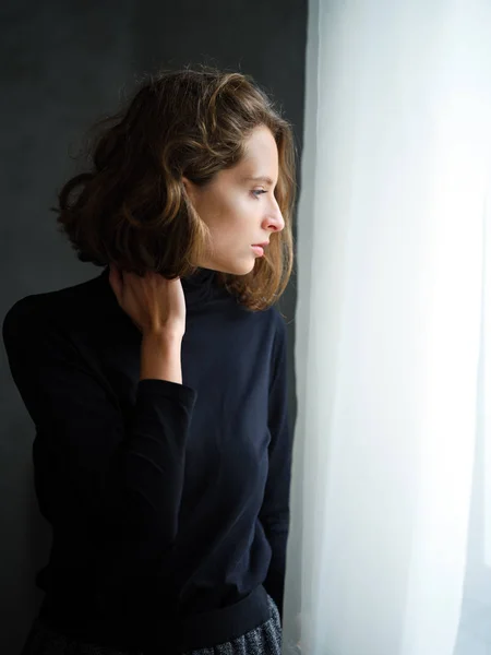 Chica pensativa en jersey negro cerca de la ventana — Foto de Stock