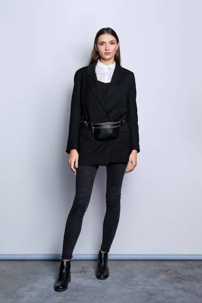 Full length portrait of trendy girl in black jacket, jeans, white shirt and waist bag — Zdjęcie stockowe