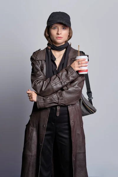 Dziewczyna w nieformalnym stroju - długi skórzany płaszcz, czarne dżinsy, bluzka, jedwabny szalik i czapka bazowa — Zdjęcie stockowe