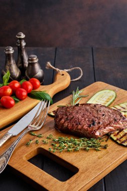 Biftek ve kabak taze domates, kiraz ve ahşap kesme tahtasında fesleğen ile servis edilir.