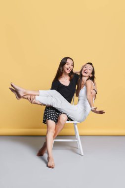 İki mutlu kız kardeş aynı sandalyede oturuyor.