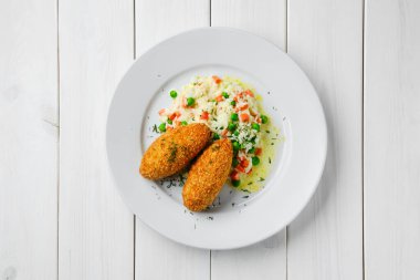 Pirinçle doldurulmuş pirzola, pirinç, yeşil bezelye ve beyaz ahşap masada havuç.