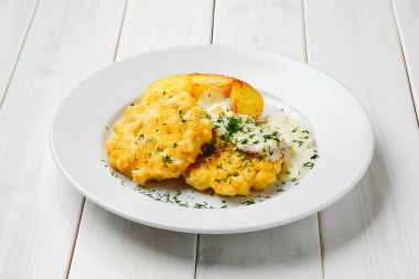 Kızarmış patates dilimleri ve beyaz ahşap masada pastırmalı kremalı soslu tavuklu pirzola.