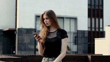 Pozitif genç kadın elinde akıllı telefonuyla bankta oturuyor.