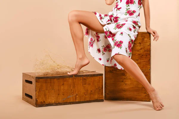 Bej arka planda, elma kutusunun üzerinde uzun bir elbise giymiş çıplak kadın bacakları.