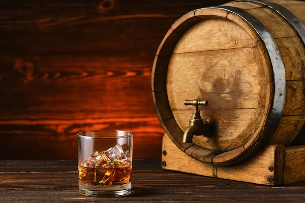 Arka planda fıçı olan buzlu bir bardak viski.