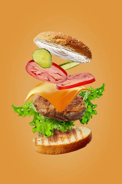 Burger with flying ingredients isolated on orange background