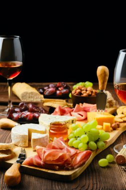 Prosciutto, üzüm, bal, hurma, kraker, fındık ve şarapla dolu bir tabak.