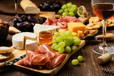 Tahta bir arka planda jambon, üzüm, bal, hurma, kraker ve şarap tabağı (ön planda odaklan)