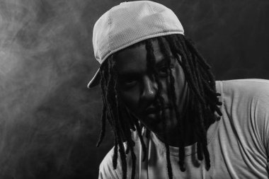 Stüdyoda kameraya poz veren bir adamın siyah beyaz portresi dumanlı bir arka planda. Kendinden emin ve ciddi bir genç adam..