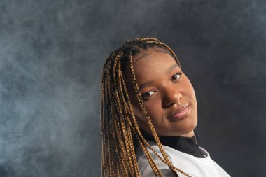 Saçları örgülü, beyaz elbiseli ve stüdyo fotoğrafı için poz veren güzel bir genç kadının portresi. Dumanlı bir arka planda izole edilmiş. Fotoşop.