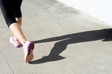 Bir insanın alt kısmı ve gölgesi, güçlü güneş ışığı altında sahil boyunca koşuyor. Sağlıklı spor pratiği. Brezilya.