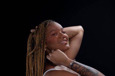 Salvador, Bahia, Brezilya - 30 Ağustos 2025: Saçları örgülü genç bir kadın siyah bir arkaplana karşı stüdyo fotoğrafı için poz veriyor. Salvador, Brezilya.