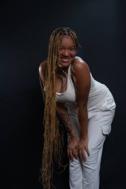 Salvador, Bahia, Brezilya - 30 Ağustos 2025: Örgülü saçlarıyla öne doğru eğilen genç bir kadın siyah bir arkaplana karşı bir stüdyo fotoğrafı için poz veriyor. Salvador, Brezilya.