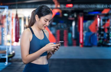 Asyalı kadınlar egzersiz sırasında cep telefonu kullanırlar. Ayakta duruyor, mesajlar yazıyor, sohbet ediyor ve mutlu bir şekilde gülümsüyor. Egzersiz yaparken spor salonu geçmişi bulanıklaşıyor ve boşlukları kopyalıyor.