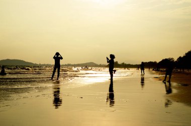 Sahilde dikilen birçok insanın silueti.