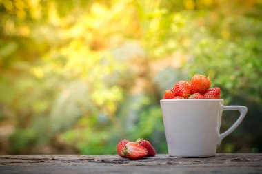 Beyaz fincanda taze çilek ve eski ahşap masada doğal ışık arka planında çilek.