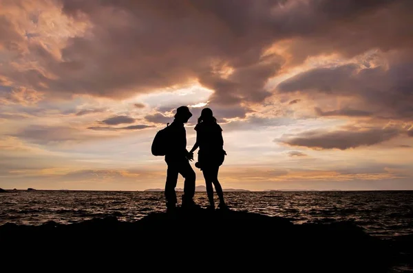 夕暮れ時にビーチで手をつないでいるカップルのシルエット — ストック写真