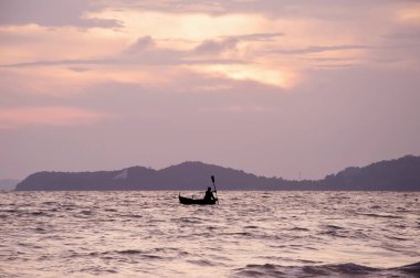 Gün batımında denizde kürek çeken insanların silueti.