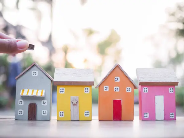 Minyatür eve bozuk para koyarken elinizi kapatın. Ev için para biriktirme kavramı, emlak yatırımları, ev kredisi, gayrimenkul..