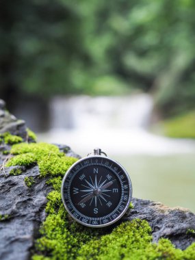 Arka planında şelale olan bir pusula. Dünya turizm günü konsepti, doğru yönleri aramak ve seyahat etmek.
