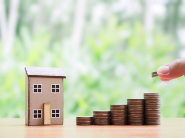 El, madeni para ve minyatür eve para koyuyor. Ev için para biriktirme kavramı, emlak yatırımları, ev kredisi, gelecekte gayrimenkul.