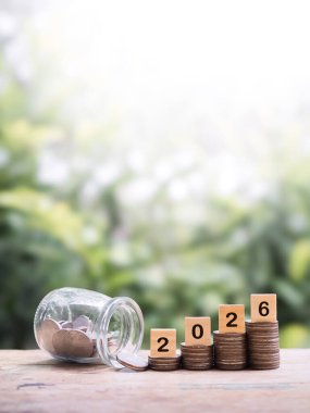 Yığınla bozuk para üzerinde 2026 numaralı tahta bloklar. 2026 yılında para, finans, yatırım ve işletme tasarruf kavramı büyüyor.