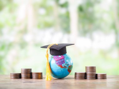 Mezuniyet şapkası ve bozuk paralarla dolu bir dünya küresi. Eğitim için para biriktirme kavramı, öğrenci kredisi, burs, gelecekte öğrenim ücretleri