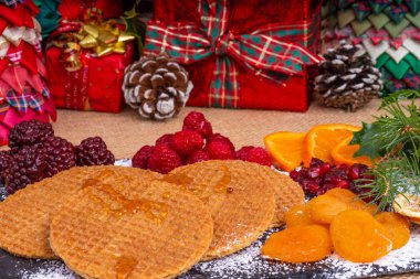 Üzerinde gözleme bisküvi akçaağaç şurubu ile kayrak bir tepside akçaağaç Syrup.Toffee Waffle bisküvi ile drizzled. Taze ve kurutulmuş meyve süslemeleri ve Noel hediyeleri bir seçim ile çevrili.