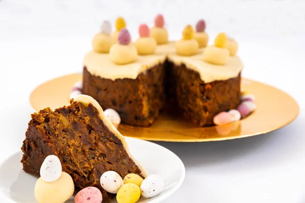 Easter Simnel Cake.  Slice of Easter Cake, also known as Simnel cake with marzipan topping and eleven balls of marzipan representing the twelve apostles minus Judas. Mini chocolate Easter Eggs round the base. Focus on the slice.