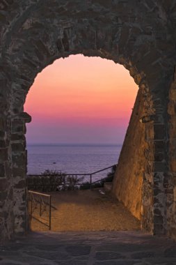 View of the sea with the bright colors of the sunset from the entrance arch of the castle of Castiglione della Pescaia clipart