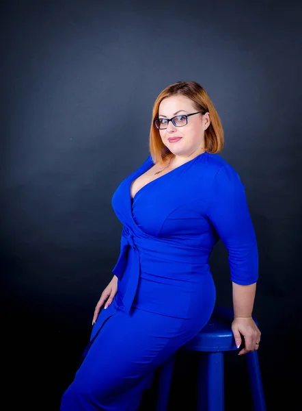 Beautiful chubby girl in blue elegant dress on a black background. Sexy plus size woman