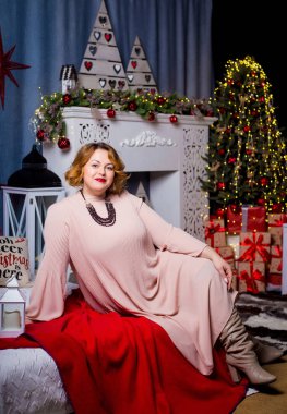 Uzun pembe elbiseli güzel bir tombul kız yeni yıl süslemeleri ile dekore edilmiş bir odada bir yatakta yatıyor.