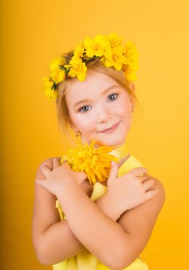 Çiller ve başında sarı bir çelenk ile şirin bir kız portresi. Sarı bir çiçek tutan sarı elbiseli bir kız
