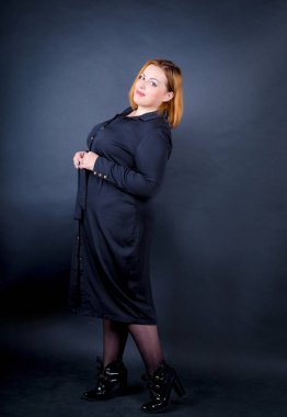 Karanlık bir arka plan üzerinde siyah elbiseli güzel tombul kız. Kendine güvenen artı boyutu kadın gözlük ve çerçeve içinde poz siyah elbise