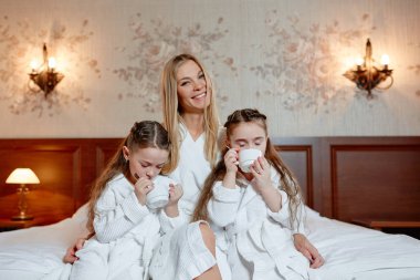 Mutlu aile, anne ve kızları İkizler, otur ve rahat oda bir yatakta dinlenin