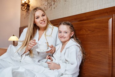 Gülümseyen anne ve çocuk yatakta rahat bir otelde kahvaltı var 