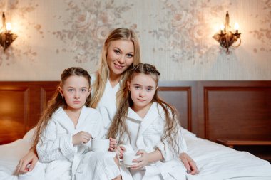 Mutlu aile, anne ve kızları İkizler, otur ve rahat oda bir yatakta dinlenin