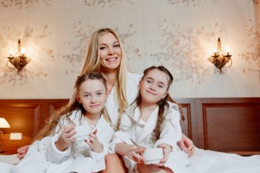 güzel ve mutlu anne ve iki kızı, kucaklamak ve gülmek. Otur ve rahat oda bir yatakta dinlenin. Kahvaltı.