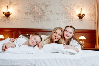 Sabahlıklar, yatağı üzerinde oynarken evler içinde iki kızı annesiyle. Mutlu aile neşeli eğlence. Öpüyor, kucaklar, çocuk annesine sevgisi